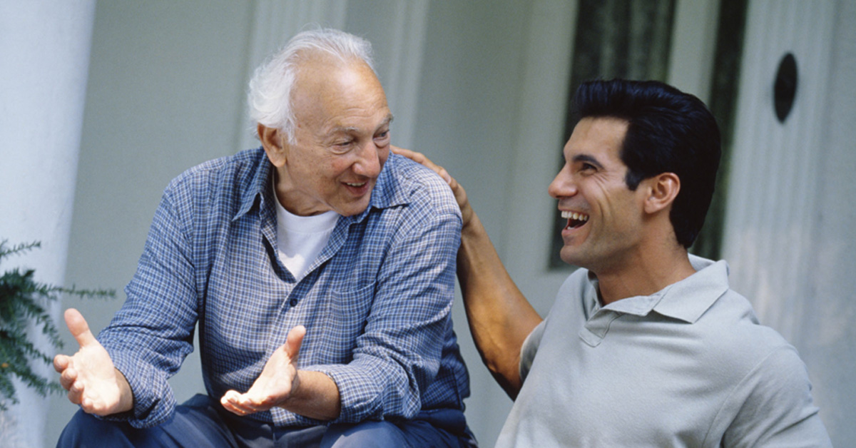 Health Benefits of Laughter, picture of and elderly caucasian male and a younger caucasian male talking and laughing together.