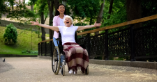 Long-Term Happiness. Picture of a younger caucasian female pushing an elderlysmiling caucasian female who is in a wheelchair.