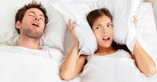 Snoring? Trouble Sleeping? Try Exercise. Picture of a caucasian male sleeping in bed and a caucasian female in bed holding her pillow around her ears.