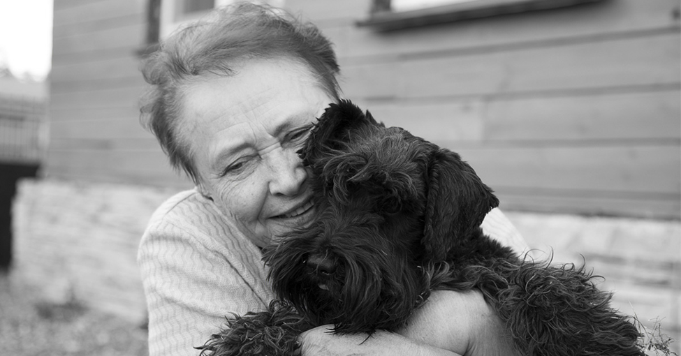 Pet Ownership and Effect on Mental Health in Seniors. Picture of an elderly caucasian female hugging a small black dog.