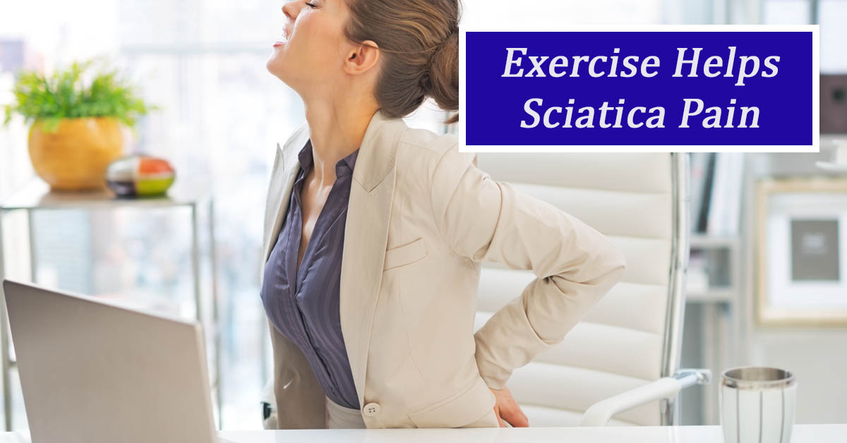 Exercises for Sciatica. Picture of a young caucasian female sitting at an office desk holding her lower back in pain.